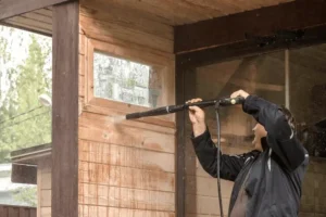 Man cleaning exterior walls and concrete flooring with a high-pressure washer.